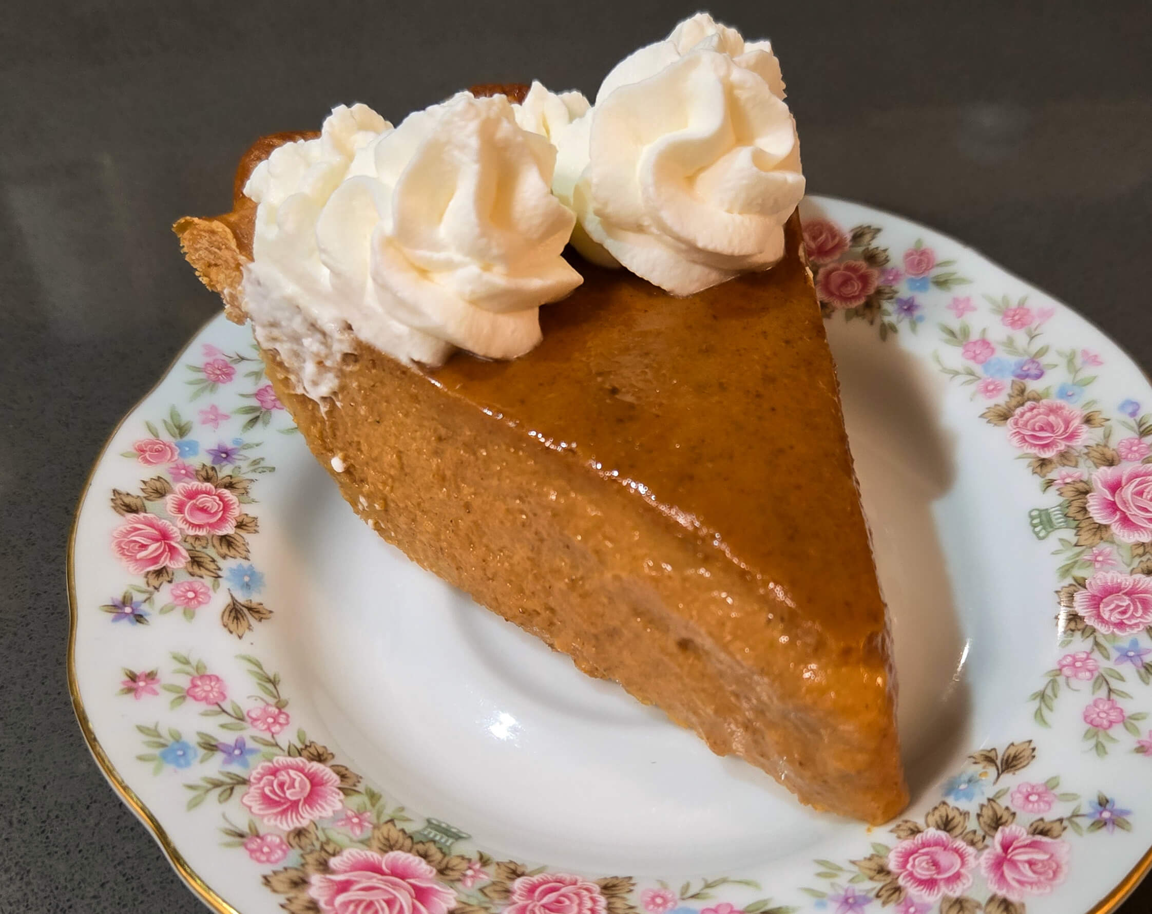close up photo of a slice of classic pumpkin pie on a floral plate in a flaky crust with whipped cream rosettes