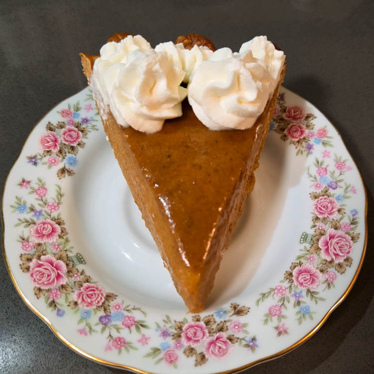 close up photo of a slice of classic pumpkin pie on a floral plate in a flaky crust with whipped cream rosettes