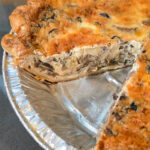 Close-up of a Mushroom Quiche in a flaky pie crust with one slice removed, revealing a creamy, golden egg custard filling packed with savory mushrooms and onions — an easy vegetarian brunch recipe perfect for Easter and weekend entertaining
