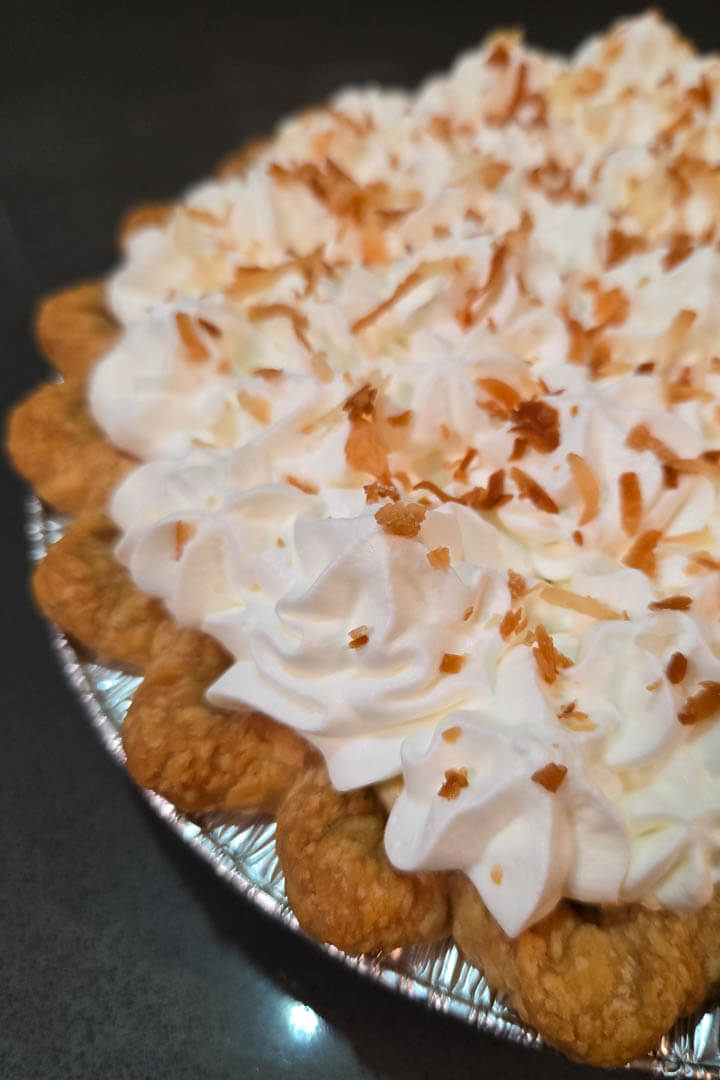 Lilikoi chiffon pie close-up photo showing a flaky crimped pie crust and piped whipped cream with toasted coconut flakes