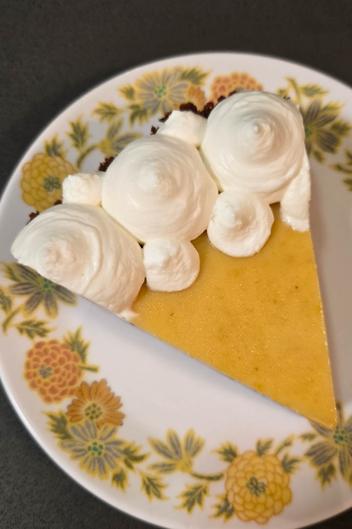 a slice of passionfruit pie on a white plate with yellow flowers topped with whipped cream swirls