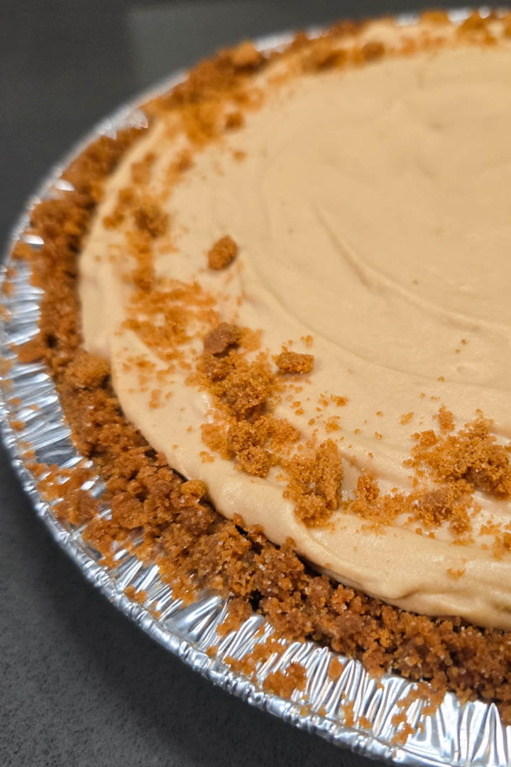 a close up photo of a no bake biscoff pie in a pie tin with cookie crumbs decorated the edges