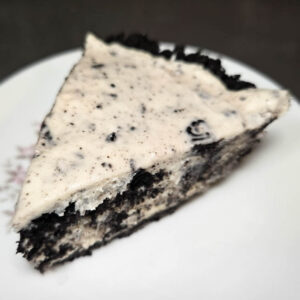 a close up photo of a slice of no bake cookies and cream pie showing creaming no bake vanilla cheesecake filling with crushed oreo cookies folded in