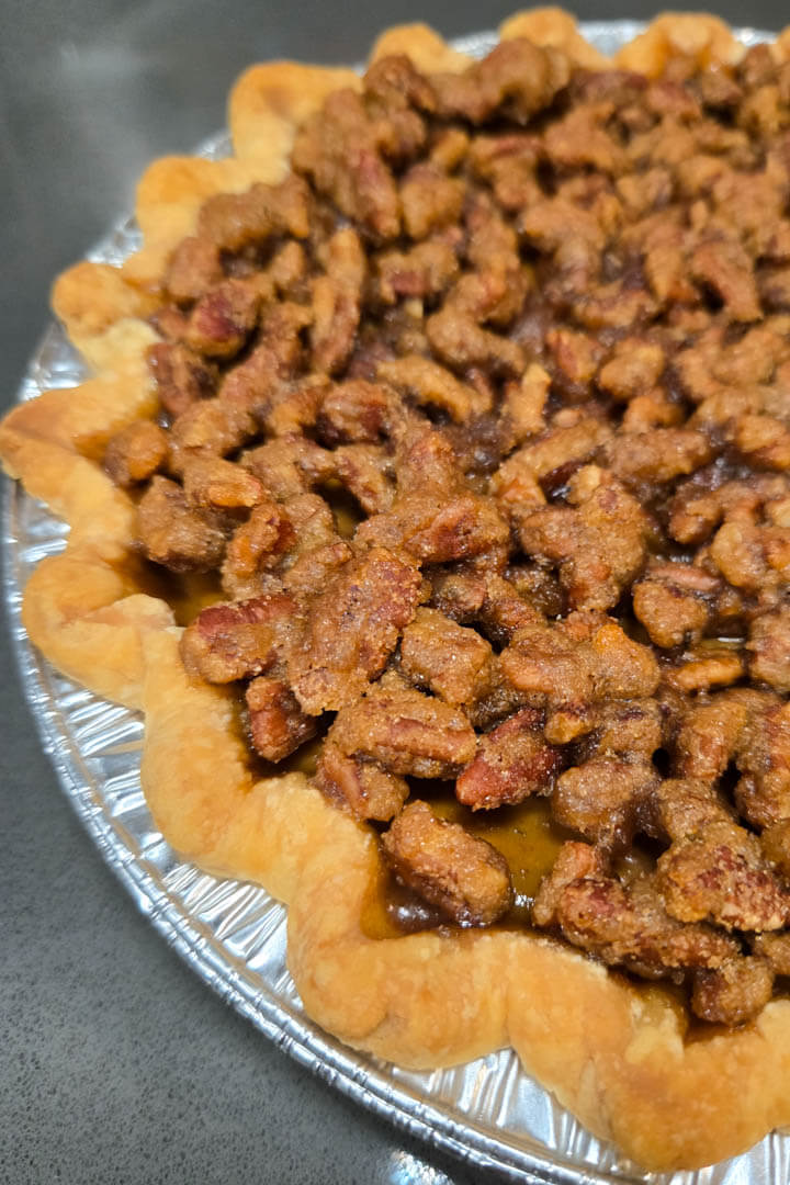 close up photo of a baked pumpkin praline pie. You can see a fluted flaky pie crust with the caramelized crunchy pecan praline topping