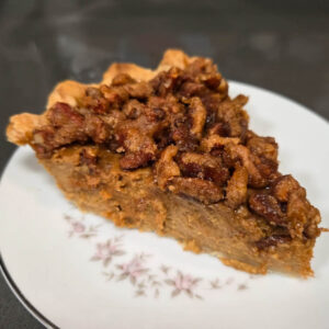 photo of a slice of pumpkin praline pie - creamy pumpkin pie filling in a flaky pie crust topped with crunchy pecan praline - on a floral plate